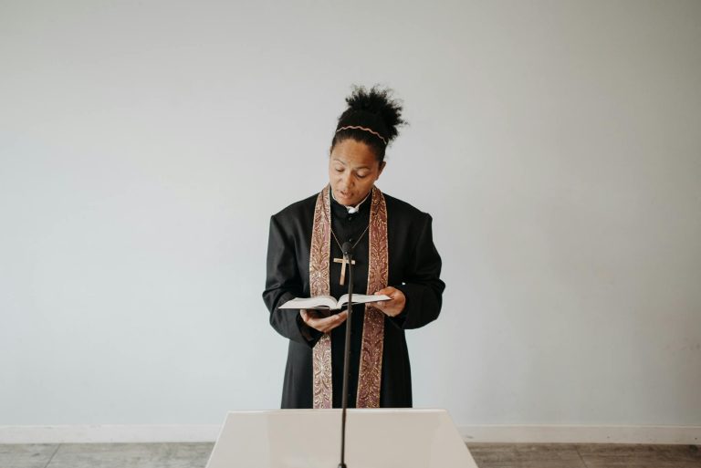A female priest in a cassock reading the Bible during a church service, conveying a serene religious atmosphere.