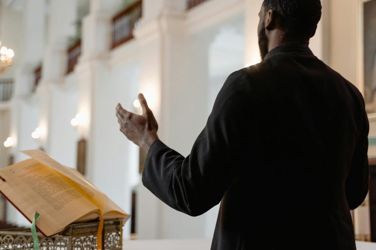 A priest delivers a sermon inside a beautifully lit church, standing at an altar.