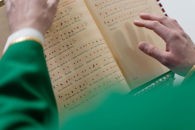 Close-up of a priest in green robes reading religious sheet music, highlighting the spirituality aspect.